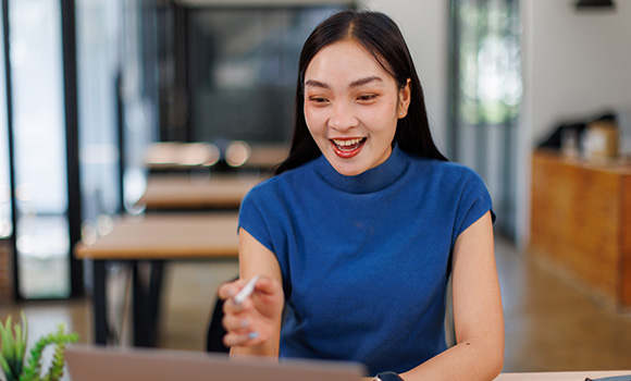 smiling woman in blue top using laptop in modern workspace engaging in conversation about 21st century technology
